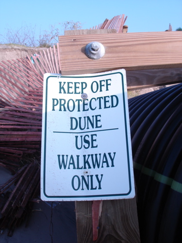 Beach warning sign beside a destroyed walkway
